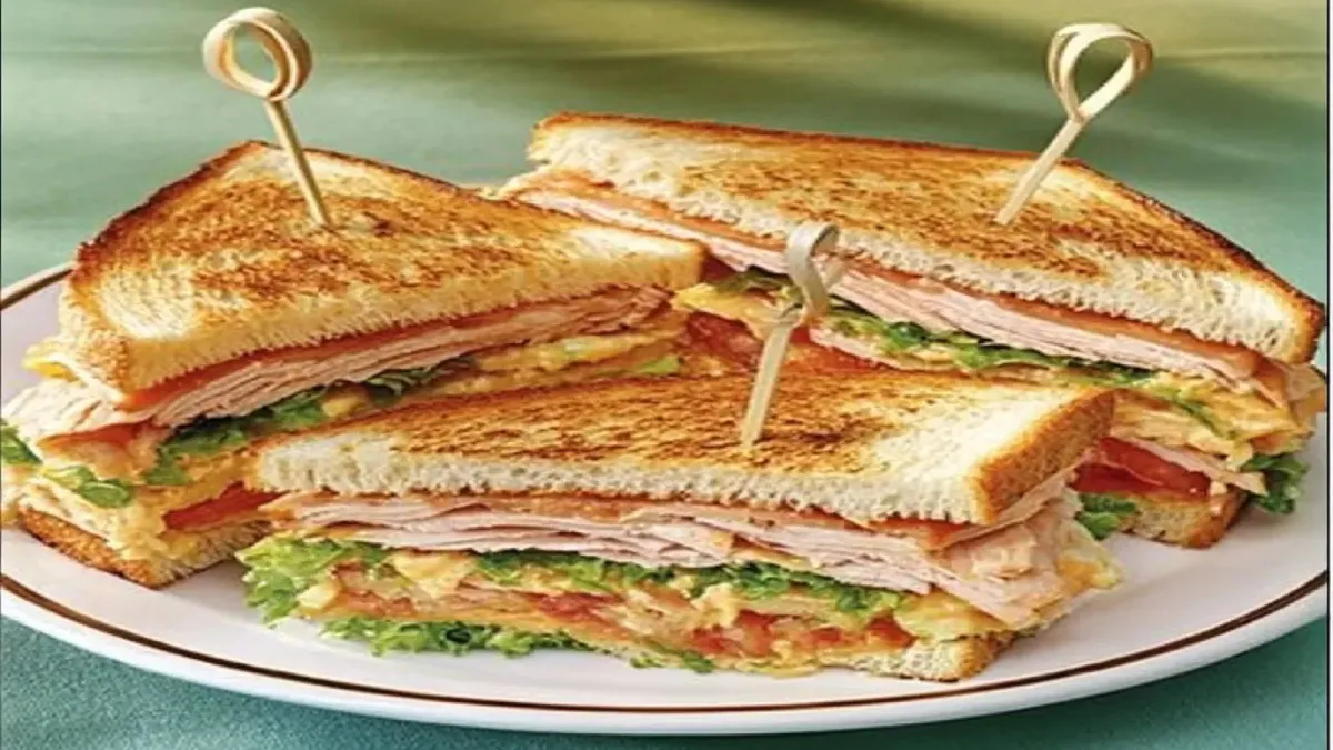 A classic turkey club sandwich stacked with turkey slices, crisp lettuce, juicy tomatoes, and creamy spread, layered between toasted bread and secured with wooden skewers.